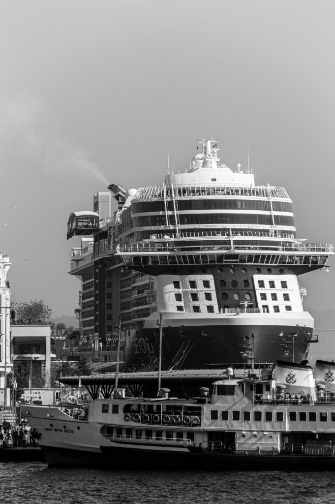 Black and white image of a large cruise ship at a bustling harbor.